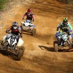 An image that showcases the vibrant Hawaiian landscape with an ATV rider navigating through lush forests, passing by a clear blue stream with majestic mountains in the background